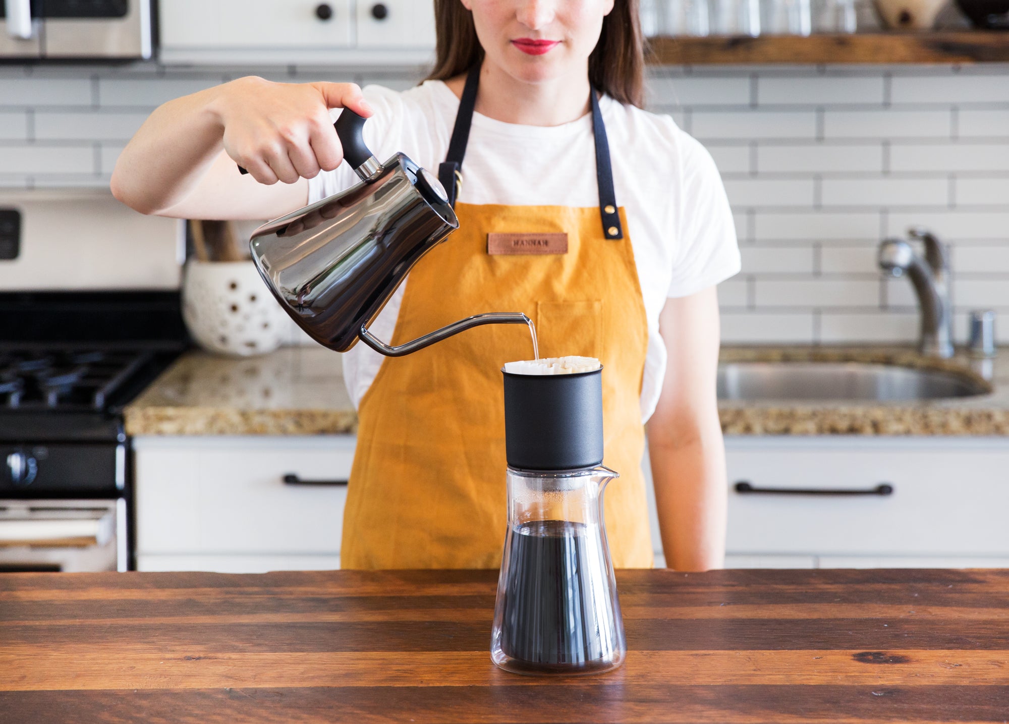 A model pours hot water out of a Fellow kettle into the Stagg Pour-Over
Dripper on a kitchen counter top.
