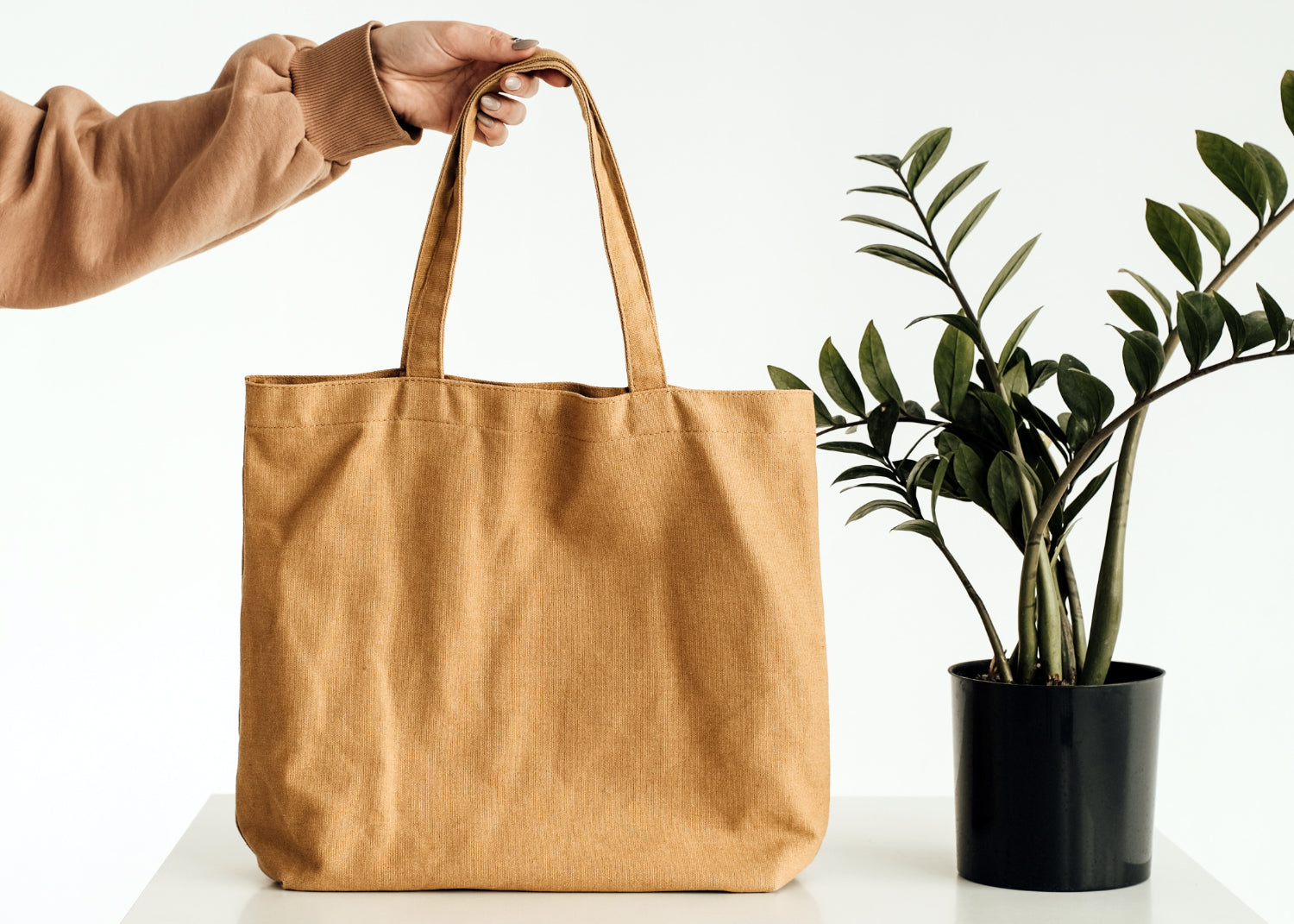 A hand demonstrates the handle of a blank tote
bag