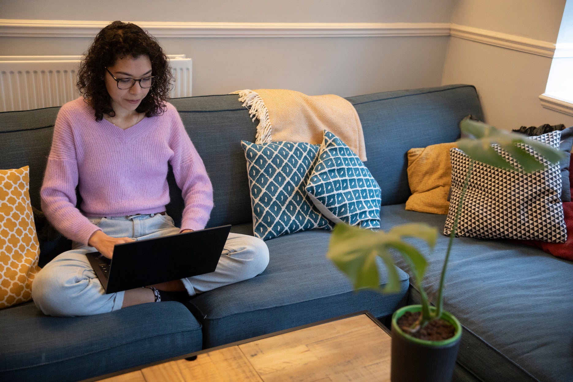 A woman sits on a blue couch typing on a
laptop