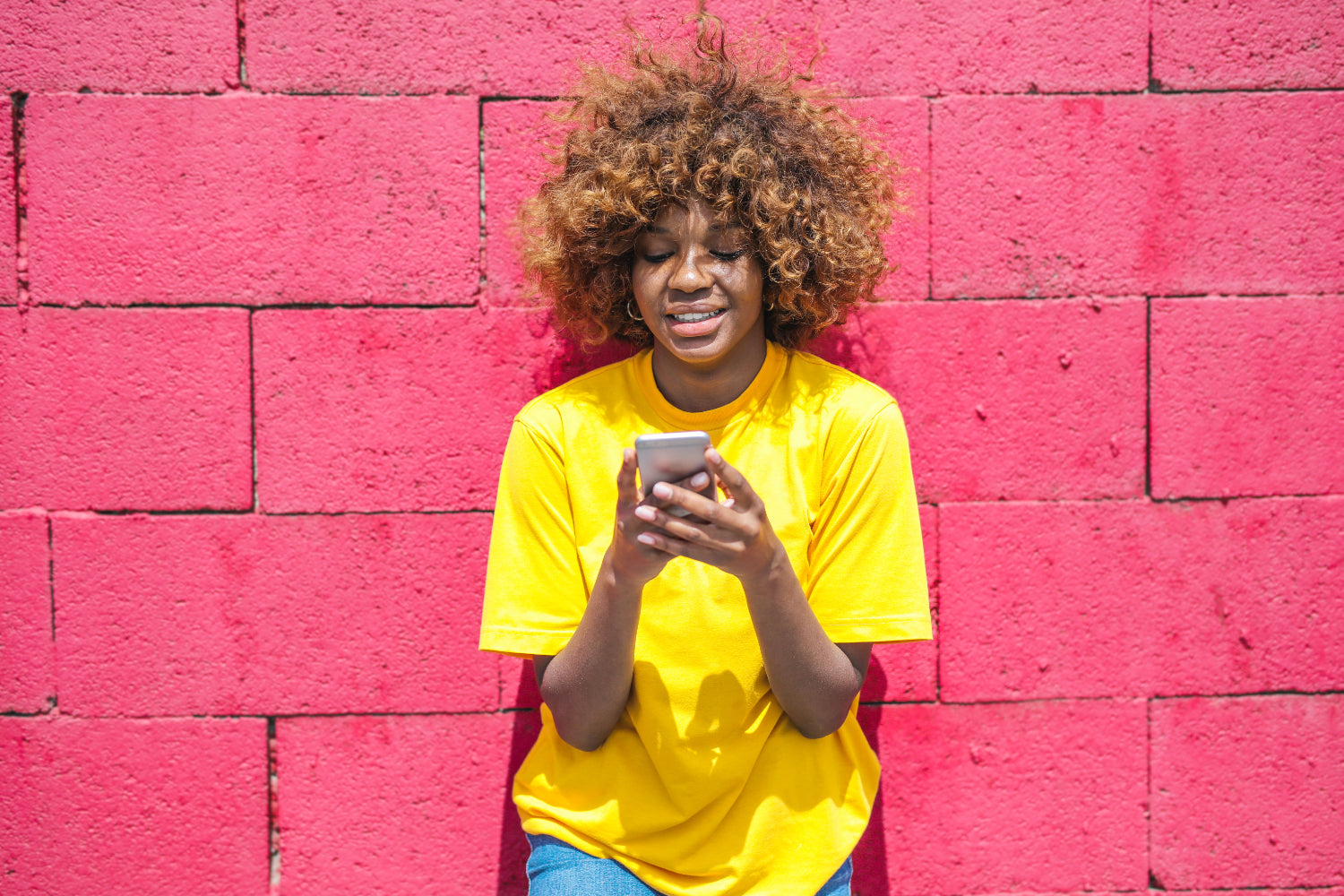 A woman leans on a pink brick wall using her
phone