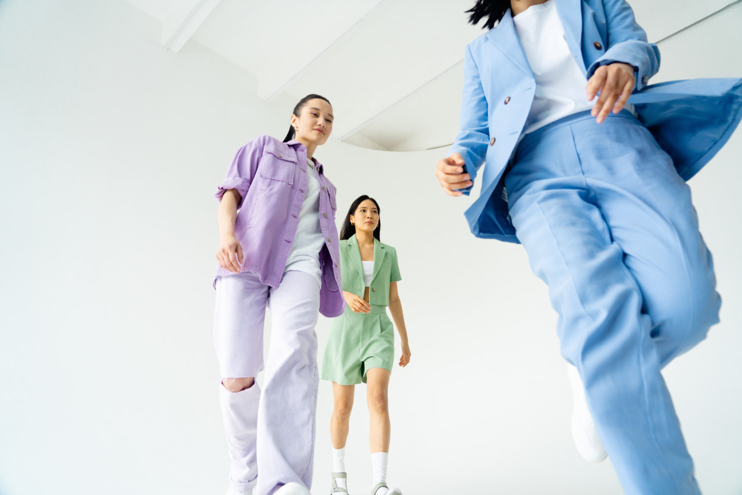 三名身穿柔和套装的年轻女性在白色房间里奔跑